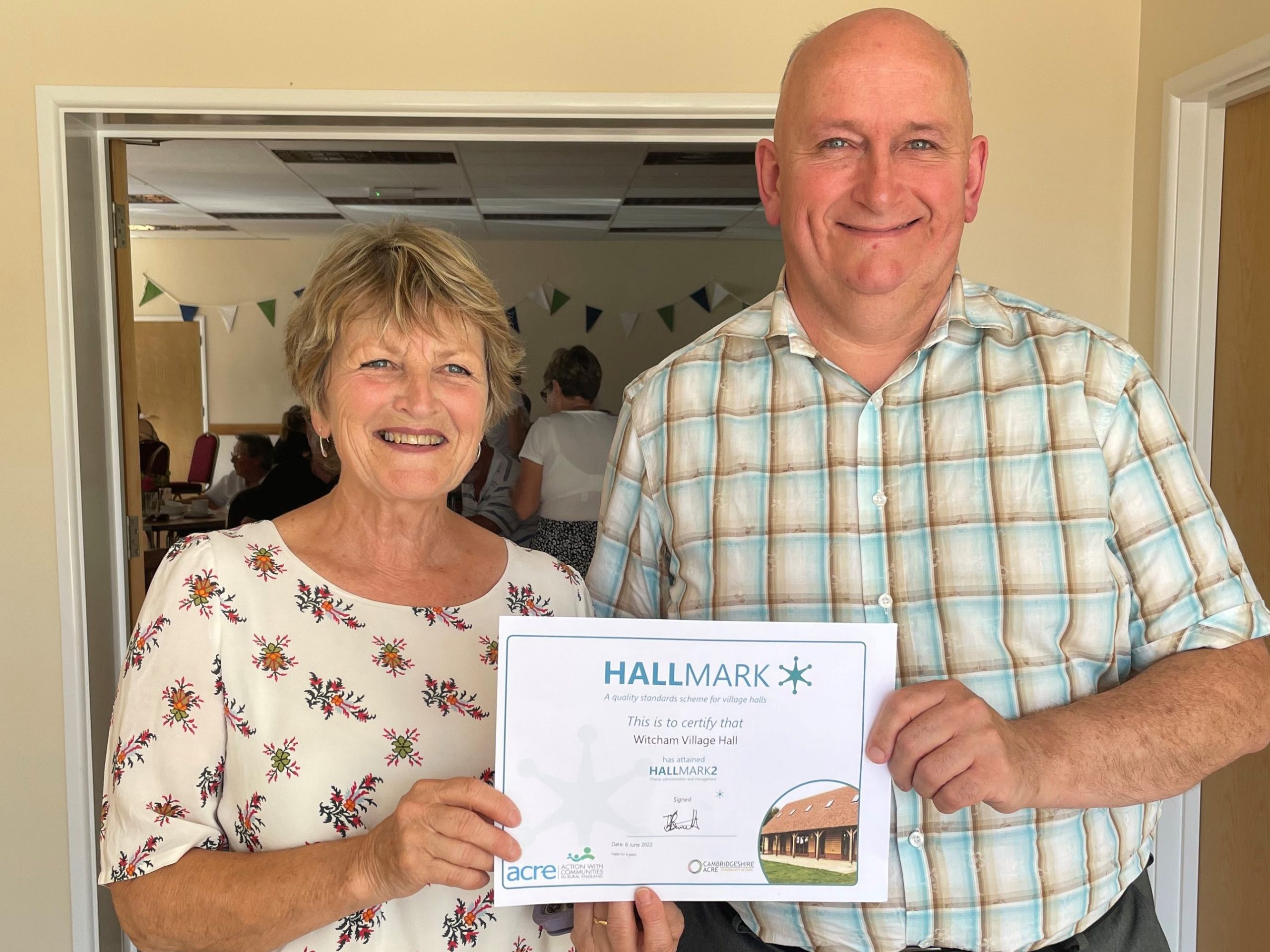 Dave Gibbs (Cambridgeshire ACRE) and Joy Walker (Witcham Village Hall) standing with the Hallmark Certificate.